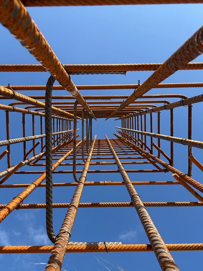Perspective view of rusted steel rebar forming a tower against a clear blue sky.